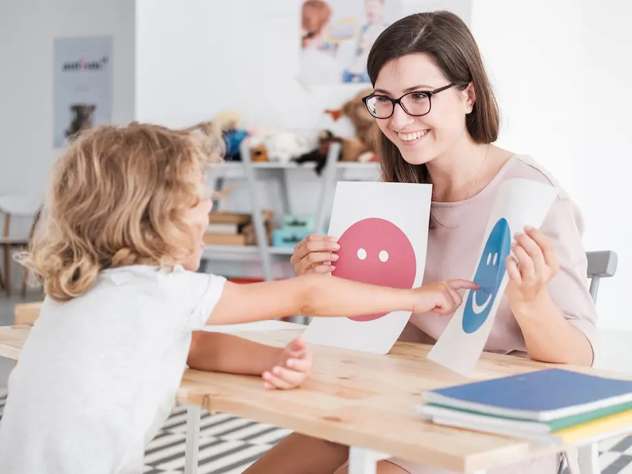 A clinician holding emotion cards with a young child during a language session